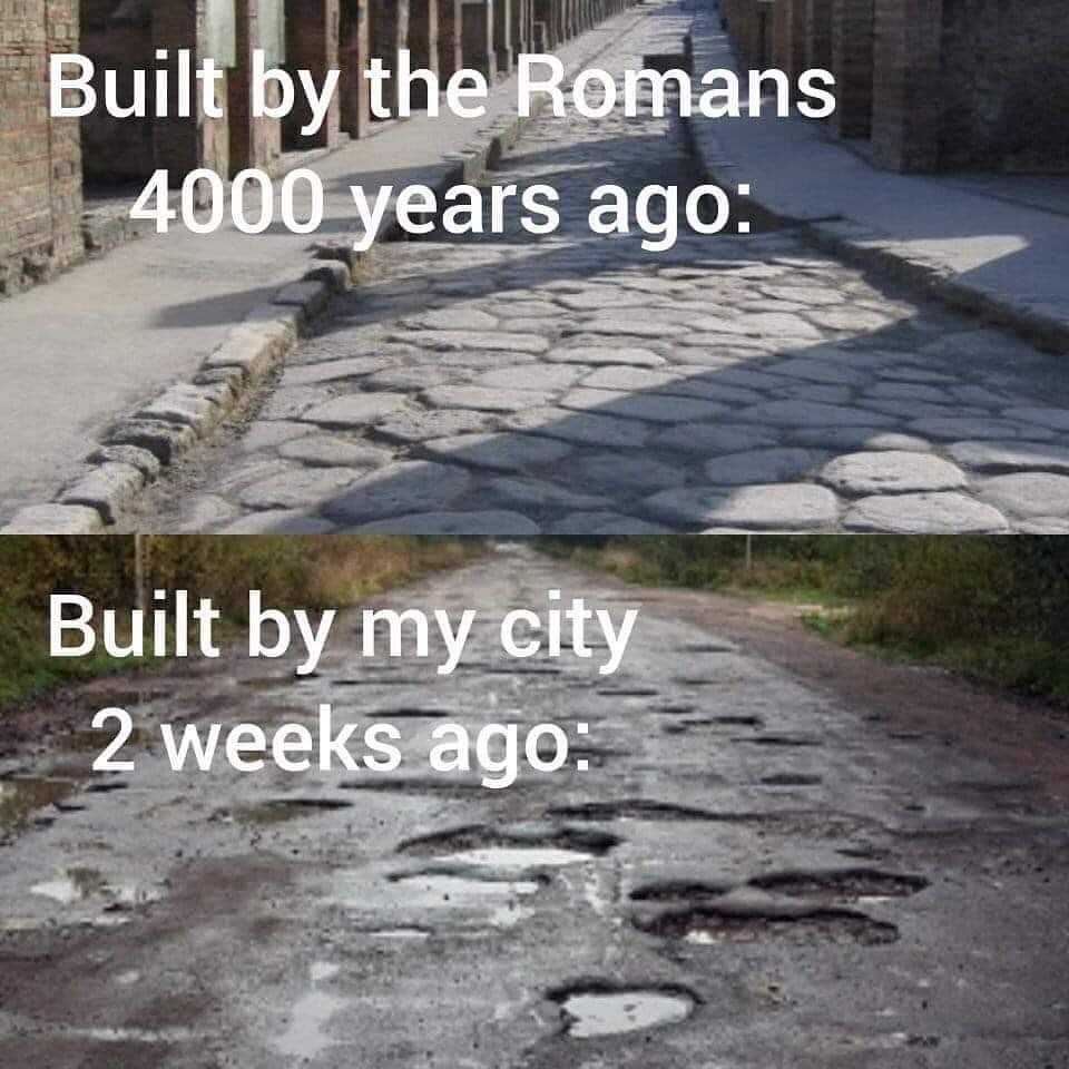 The meme is a humorous comparison between the quality of roads built by the ancient Romans and those built in modern times. The top image shows a well-maintained, ancient Roman road, while the bottom image depicts a modern road with potholes and cracks. The text reads: "Built by the Romans 2000 years ago: / Built by my city 2 weeks ago: "